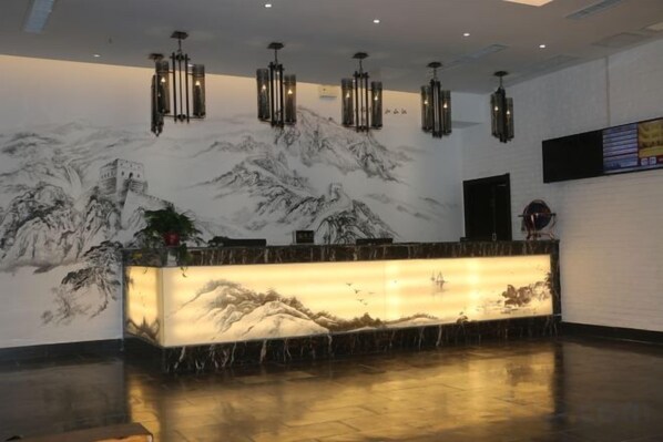 Un mostrador de recepción con un mural de montañas, iluminación colgante y una pantalla digital en la pared.