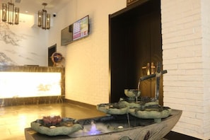 A reception area with a reception desk, a wall-mounted TV, and a decorative water feature.