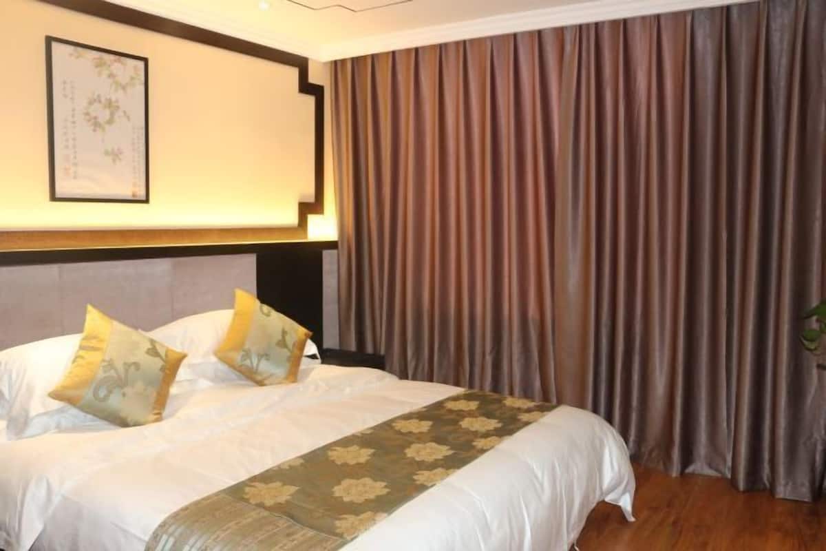 Hotellihuone, jossa on sänky, verhot, sängynpääty ja seinällä oleva kehystetty kuva.