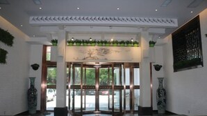 A lobby with a revolving door, potted plants, and a large wall painting. - Huaxia Jingdu Business Hotel (Taiyuan)