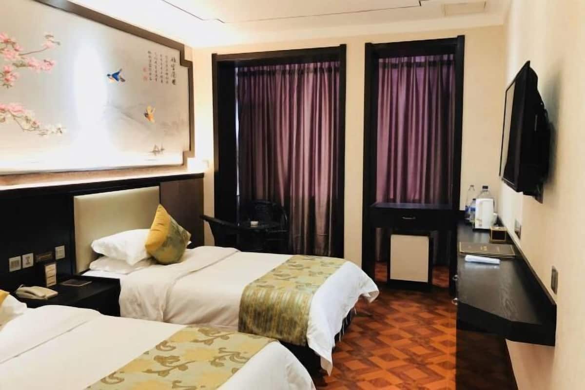 Hotellihuone, jossa on kaksi sänkyä, työpöytä, tuoli, televisio ja koristeellinen seinäelementti.