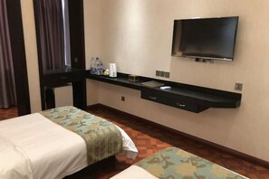 Habitación de hotel con dos camas, un televisor de pantalla plana montado en la pared, un escritorio con una silla y una mesita con una botella y una taza.