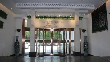 A hotel lobby with a revolving door, potted plants, and a large vase.