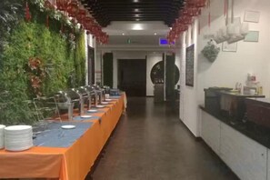 Une longue table entourée de nombreuses chaises et un buffet disposé dans un couloir d’hôtel.