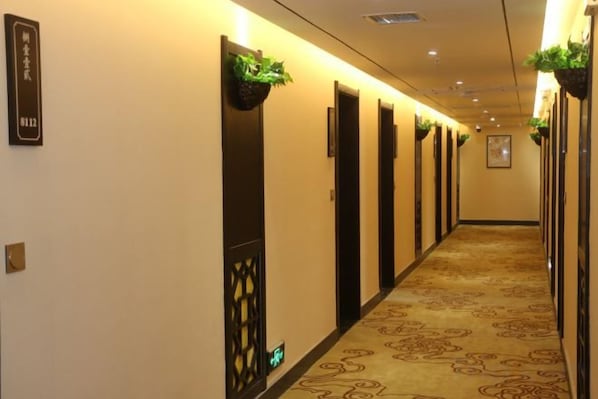 A hotel hallway with doors, carpeted floors, and wall-mounted plants.