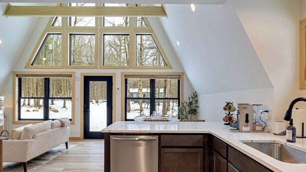 A modern kitchen with a central island, large windows, and a dining area with a sofa. -  Cozy Modern A-Frame with Hot tub, Fireplace, soak tub & Games (Albrightsville)