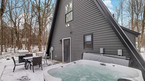 A two-story house with a hot tub in the backyard, surrounded by snow and trees. -  Cozy Modern A-Frame with Hot tub, Fireplace, soak tub & Games (Albrightsville)