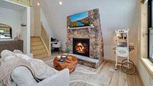 A cozy living room with a stone fireplace, a comfortable sofa, a coffee table, and a TV mounted on the wall. -  Cozy Modern A-Frame with Hot tub, Fireplace, soak tub & Games (Albrightsville)