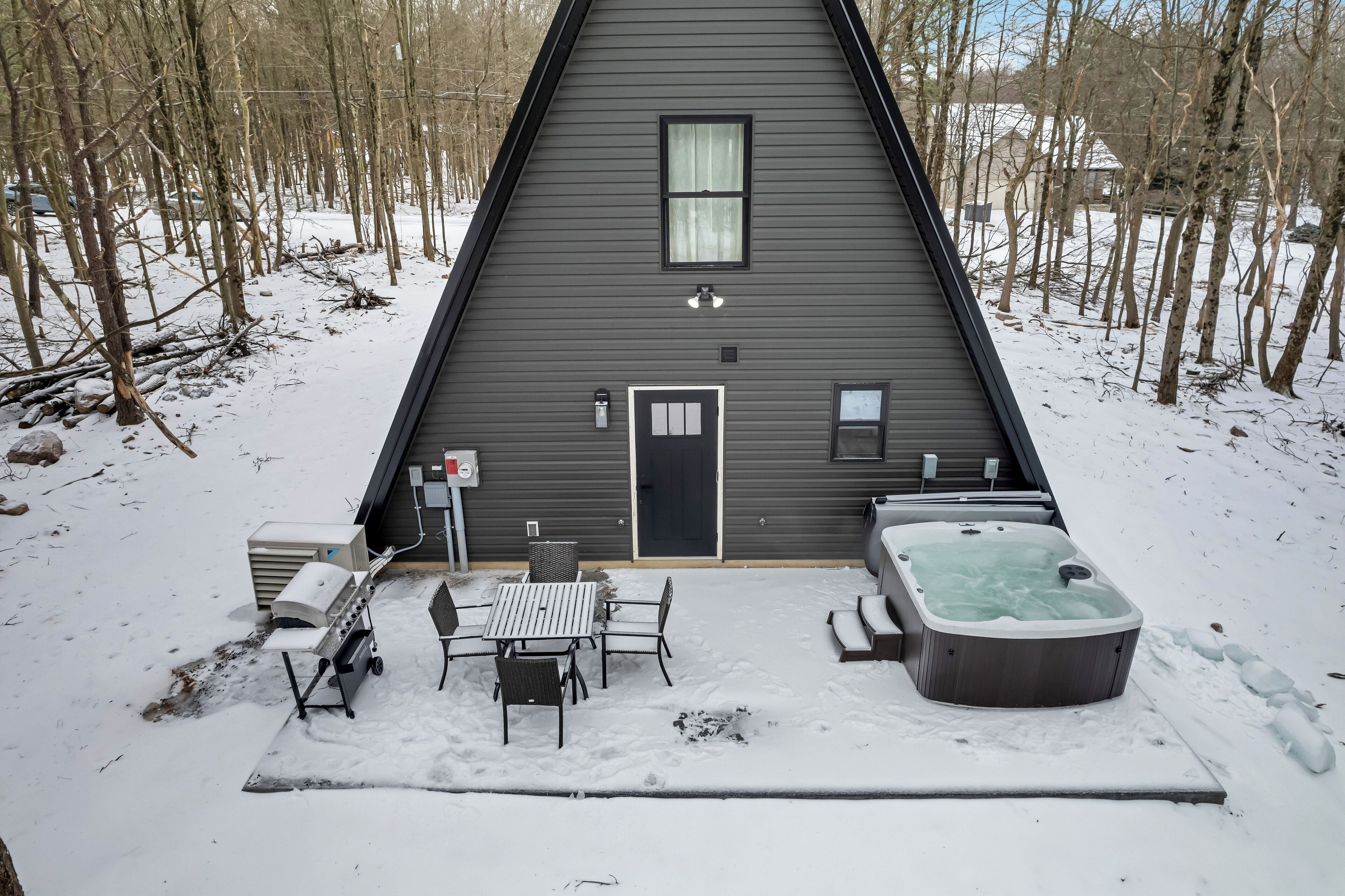 A triangular cabin with a door, a window, and a hot tub in the snow.