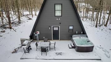 A triangular cabin with a door, a window, and a hot tub in the snow.