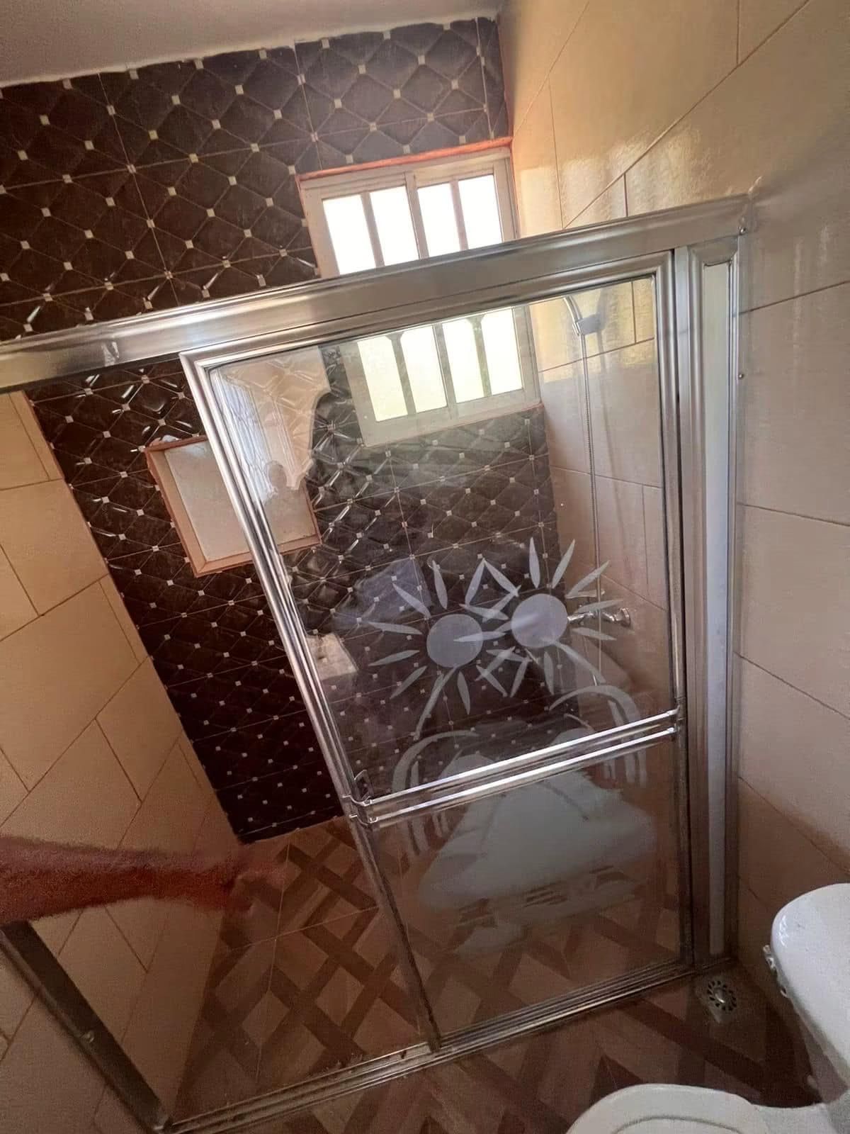 Une salle de bain avec une douche à parois de verre, un mur décoré d’un motif et une fenêtre.