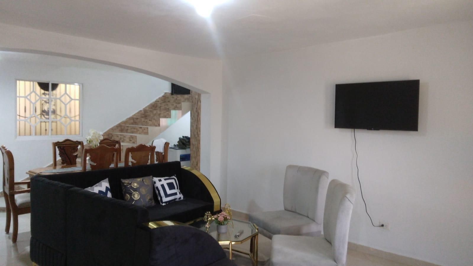 Ein Wohnzimmer mit einer Couch, einem Sessel und einem an der Wand befestigten Flachbildfernseher.