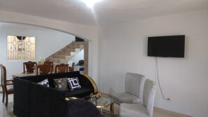 A living room with a black sofa, a grey armchair, and a coffee table. A TV is mounted on the wall.