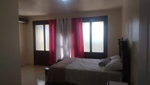 A bedroom with a bed, a nightstand, a dresser, and a window with curtains.