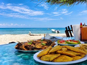 A beachside dining table with seafood dishes, a view of the ocean, and a boat in the background.