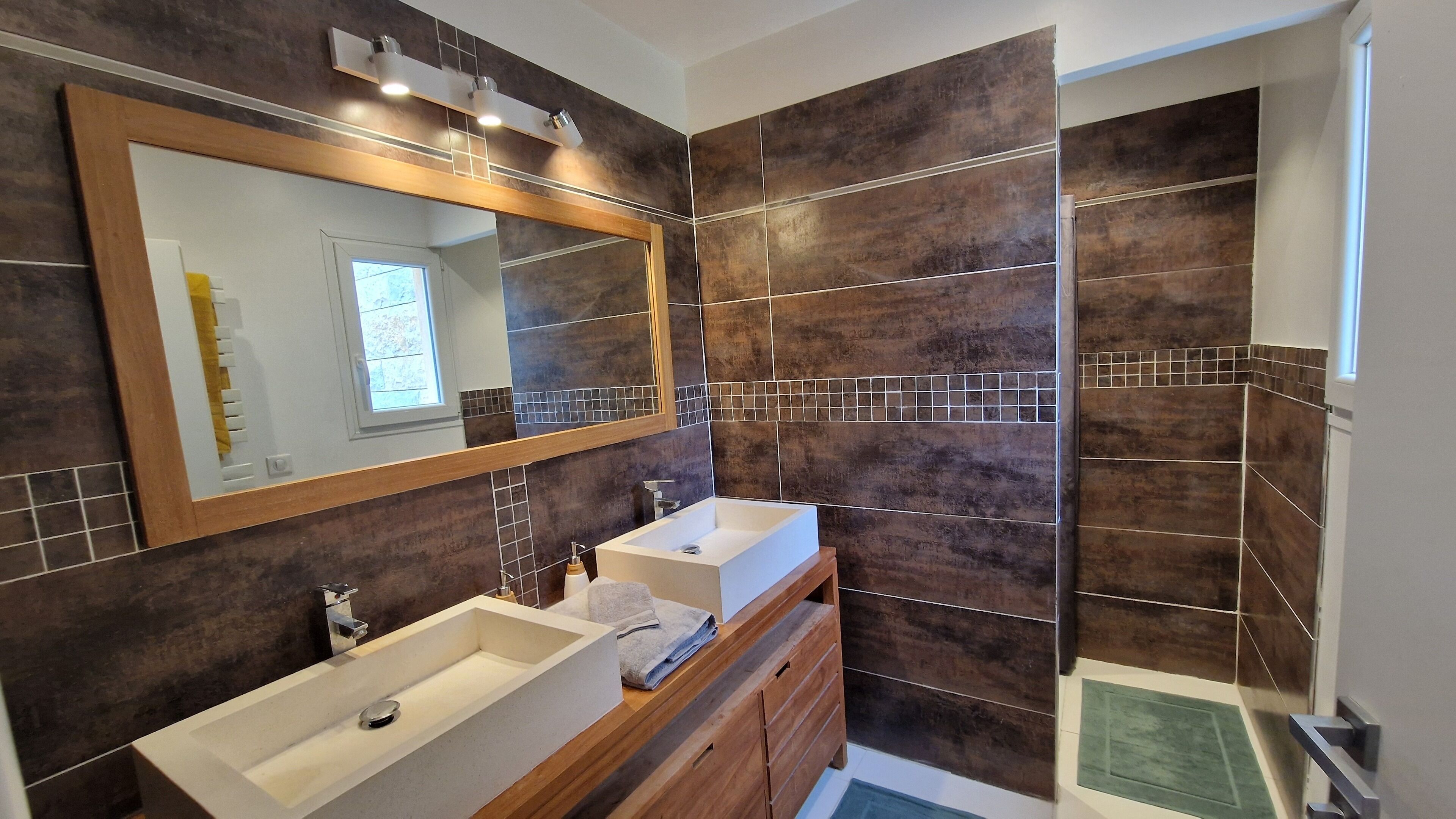 Une salle de bain moderne avec deux lavabos, un grand miroir et un espace douche.