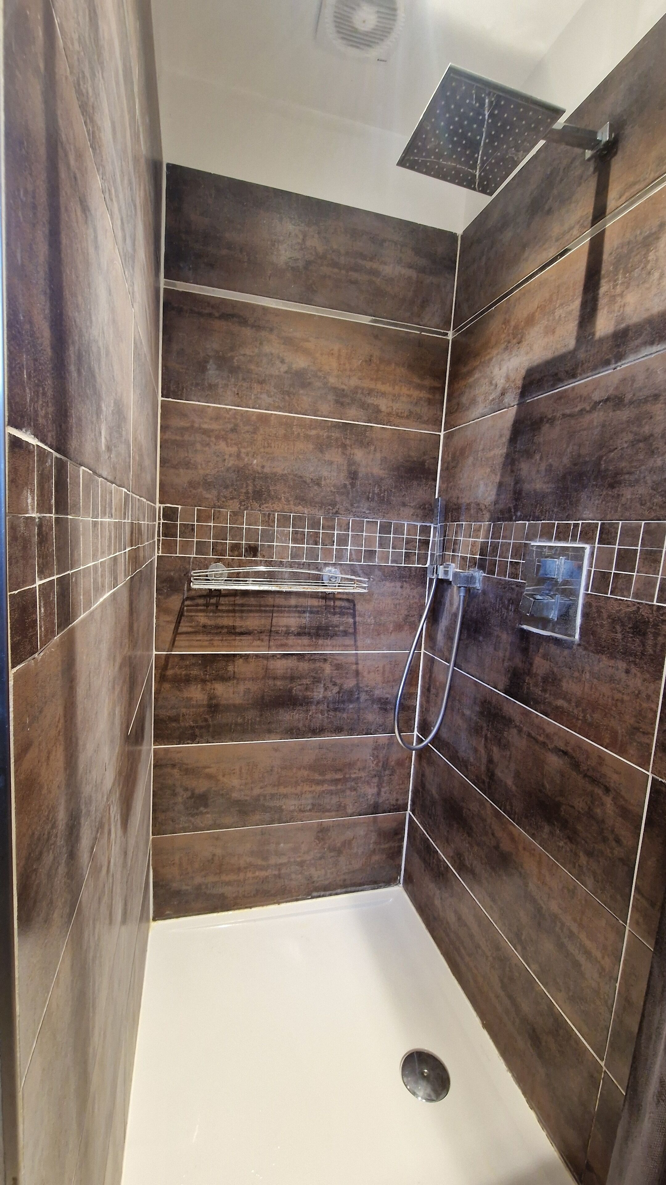A modern bathroom with dark wood paneling, a shower area, and a tiled backsplash.