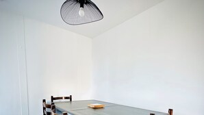 A dining area with a rectangular table, six wooden chairs with cushioned seats, a black pendant light, and a light-colored wooden floor. - Sea view villa, sleeps 4. (Asnelles)