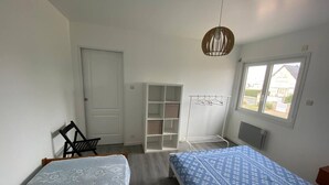 A bedroom with two beds, a wardrobe, a chair, a drying rack, and a window with a view. - Sea view villa, sleeps 4. (Asnelles)