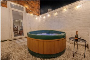 Een hottub met houten buitenkant, een fles champagne en twee glazen op een bijzettafeltje.