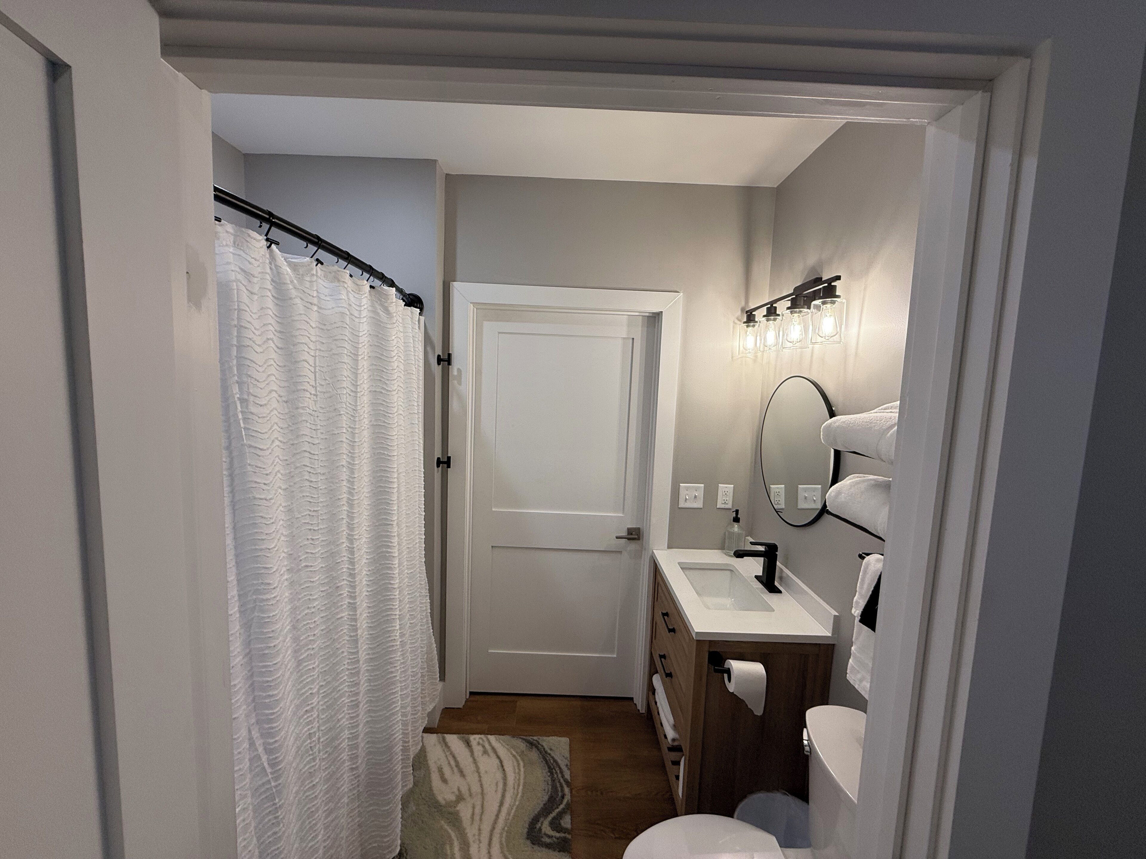 Ein kleines Badezimmer mit Duschvorhang, Toilette, Waschbecken mit Spiegel und Handtuchhalter.