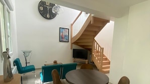 A modern living room with a dining area, a staircase, and a clock on the wall. - Le Laurier Blanc is 10 minutes from Parc Caillebotte, with its terrace for aperitifs. (Yerres)