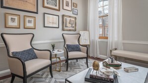 A room with two armchairs, a small round table, and a bench. The walls are adorned with framed artwork. - Step into History: Charming Fells Point Retreat (Baltimore)