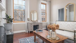 A room with a wooden dresser, a vanity with a mirror, a vase with dried flowers, and a bookshelf with books. - Step into History: Charming Fells Point Retreat (Baltimore)