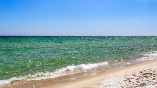 A beach with clear turquoise water, a sandy shore, and a clear sky.