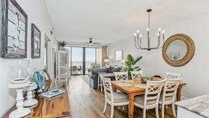 A dining area with a wooden table and white chairs, a chandelier, and a view to the outside.