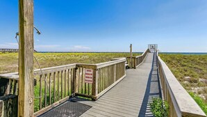 A wooden boardwalk leading to a beach with a sign indicating shoes should be worn on the walkway.