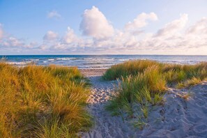 Ein Sandweg am Strand, gesäumt von Gras, der zum Meer führt.