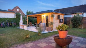 Eine Terrasse mit Grill, Topfpflanzen und draußen abgestellten Fahrrädern vor einem Haus mit überdachter Veranda.