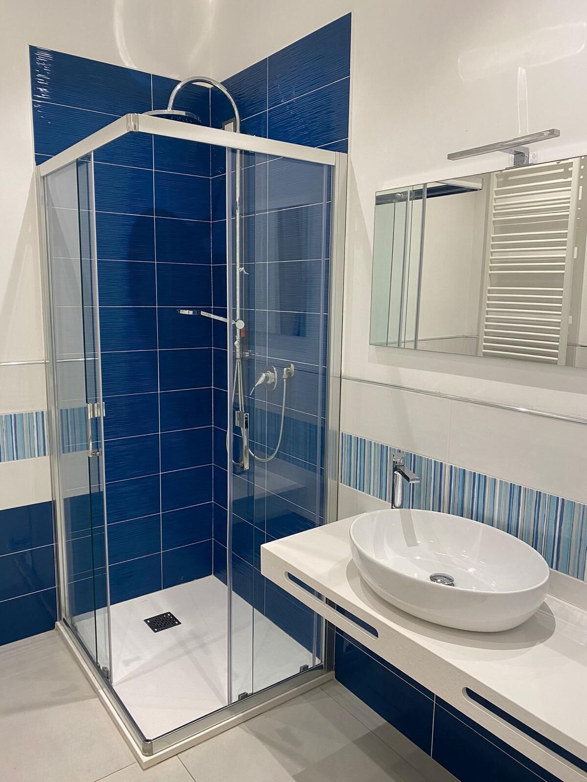 Un baño moderno con ducha de vidrio, un lavabo blanco y un espejo encima.