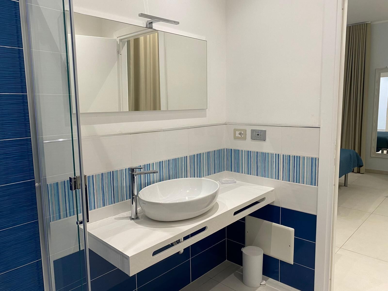 Een moderne badkamer met een witte wastafel, blauw-witte betegelde muren, een spiegel boven de wastafel en een toilet in de achtergrond.