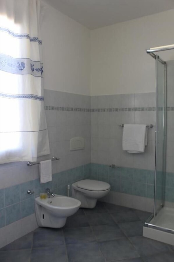 A bathroom with a bidet, toilet, and glass shower enclosure. - Hotel on the promenade of Stintino (Stintino)