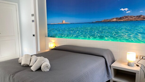 A bedroom with a bed, two bedside lamps, and a wall mural of a coastal scene.