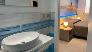A modern bathroom with a white sink, blue-striped tiles, a mirror, and a nightstand with a lamp.