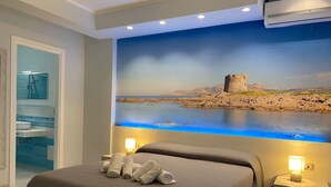A hotel room with a large bed, two bedside tables with lamps, a bathroom with a sink and mirror, and a mural of a coastal landscape.