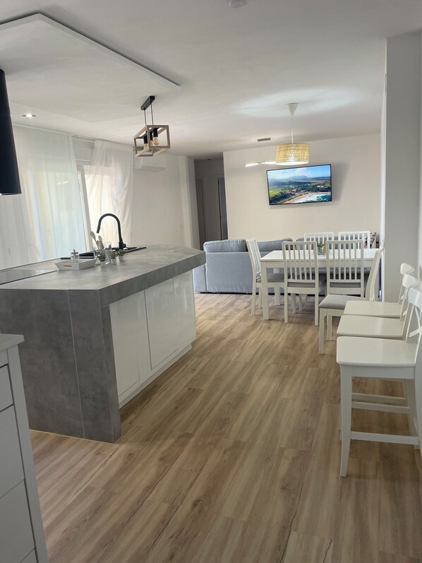 Cozinha moderna com ilha central, armários brancos e área de jantar com cadeiras e mesa brancas.