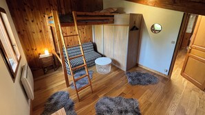 A cozy room with a bunk bed, a ladder, a small round table, fluffy rugs, and wooden walls. - Superb Chalet in a quiet location, garden and private parking, near Paris and Disney. (Fontenay-sous-Bois)