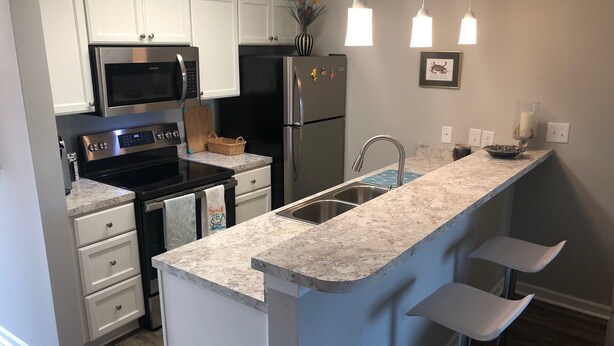 A modern kitchen with white cabinets, stainless steel appliances, a granite countertop, and a bar area with stools.
