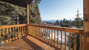 A wooden deck with a railing overlooking a snowy landscape and trees.