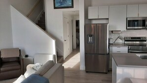 A modern kitchen with stainless steel appliances, a dining area with a white table, and a staircase leading to another level.