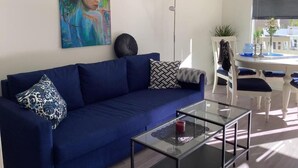 Una sala de estar moderna con un sofá azul, una mesa de centro de vidrio y un cuadro en la pared.