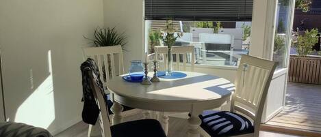 Ein Essbereich mit rundem Tisch und vier Stühlen, einer Vase mit Blumen und Blick ins Freie durch große Fenster.