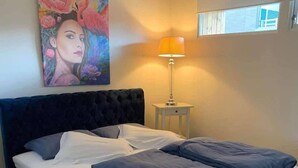 Un dormitorio con una cama grande, un cuadro en la pared, una lámpara y una ventana.