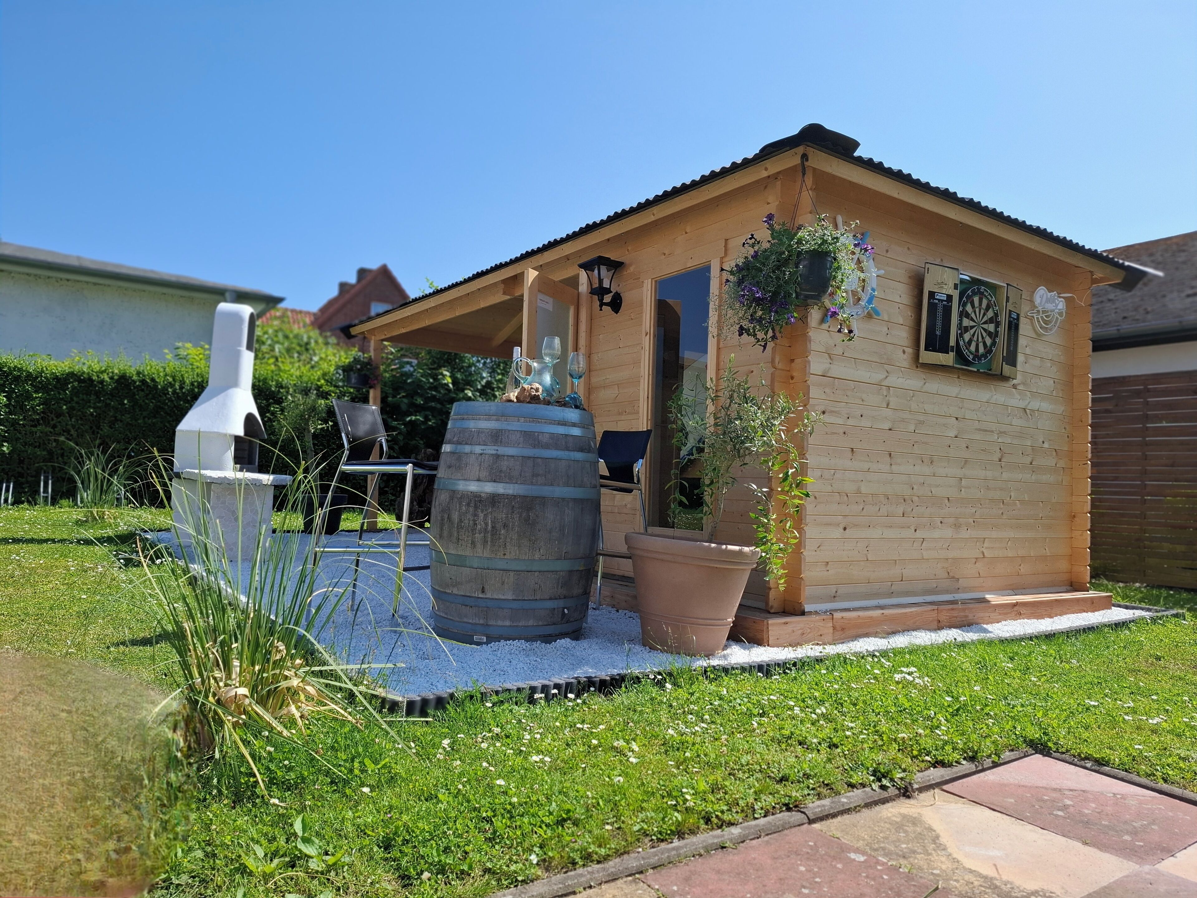 A small wooden cabin with a porch, a barbecue grill, and a dartboard.