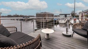 A deck with outdoor seating, a table, and a view of the water and docked boats. - Spacious 120m2 Watervilla With Sauna Near Amsterdam And Schiphol. (Aalsmeer)