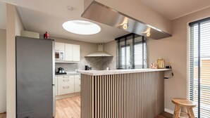 A modern kitchen with a central island, a built-in stove, and a large window with blinds. - Spacious 120m2 Watervilla With Sauna Near Amsterdam And Schiphol. (Aalsmeer)